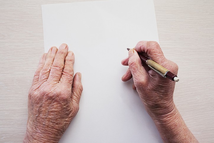 dłonie starszej osoby z długopisem w ręku nad kartką papieru